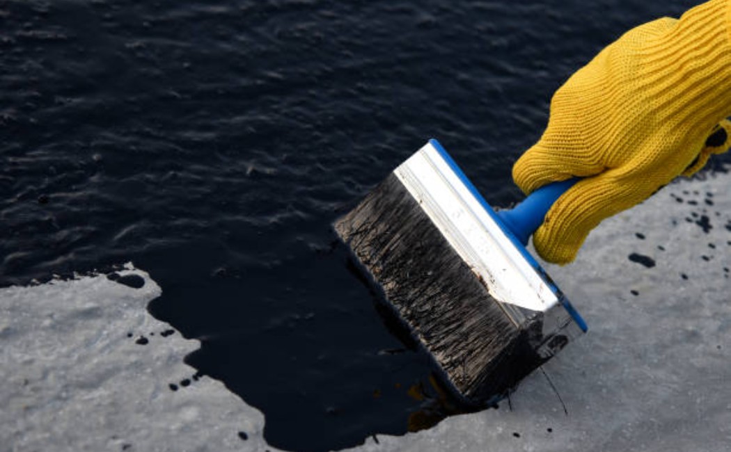 Laborer spreading waterproofing bitumen coating on building foundation