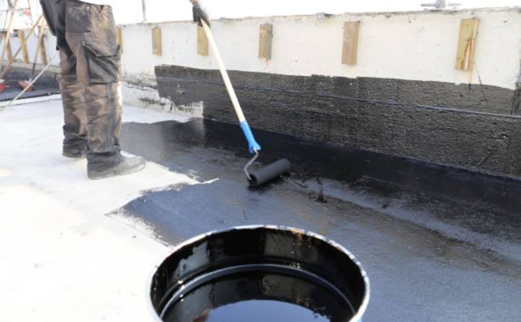 Applying bitumen sealant to a flat rooftop with a paint roller