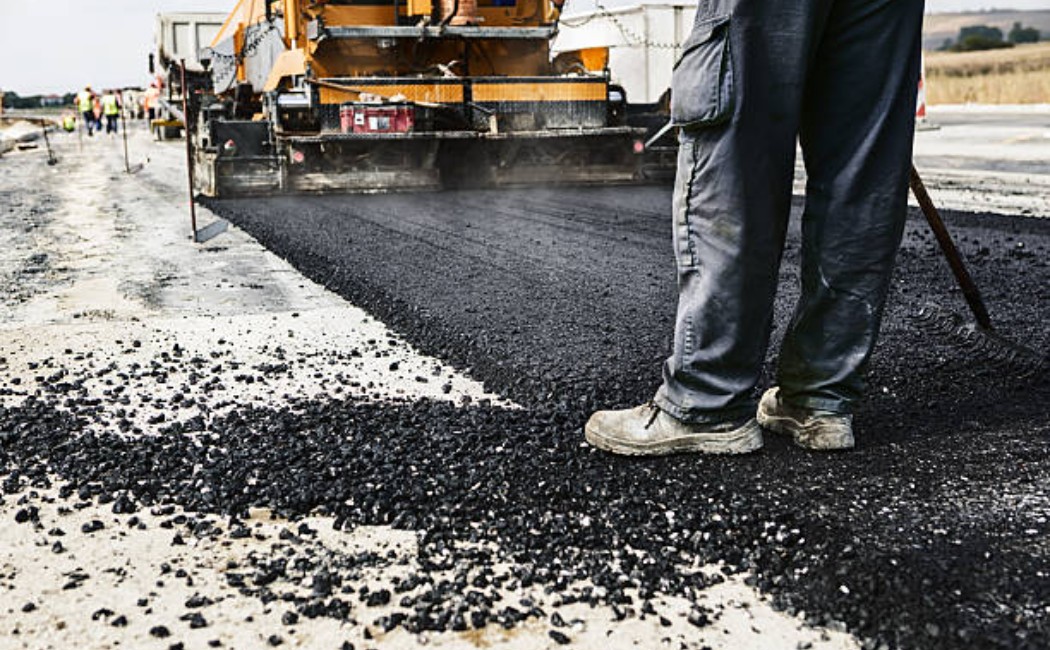 Worker standing on freshly laid asphalt during road construction