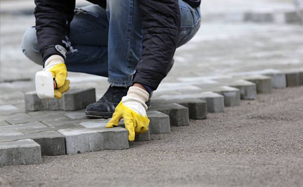 Worker in a high-visibility vest arranging large rectangular pavers.