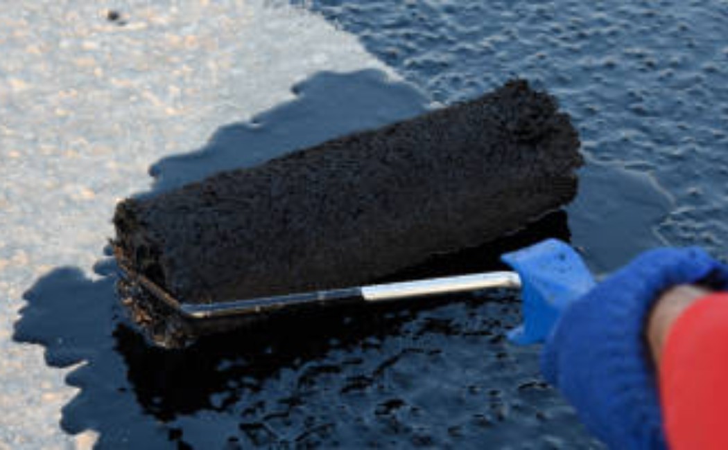 A professional applying a protective bitumen layer to the foundation wall