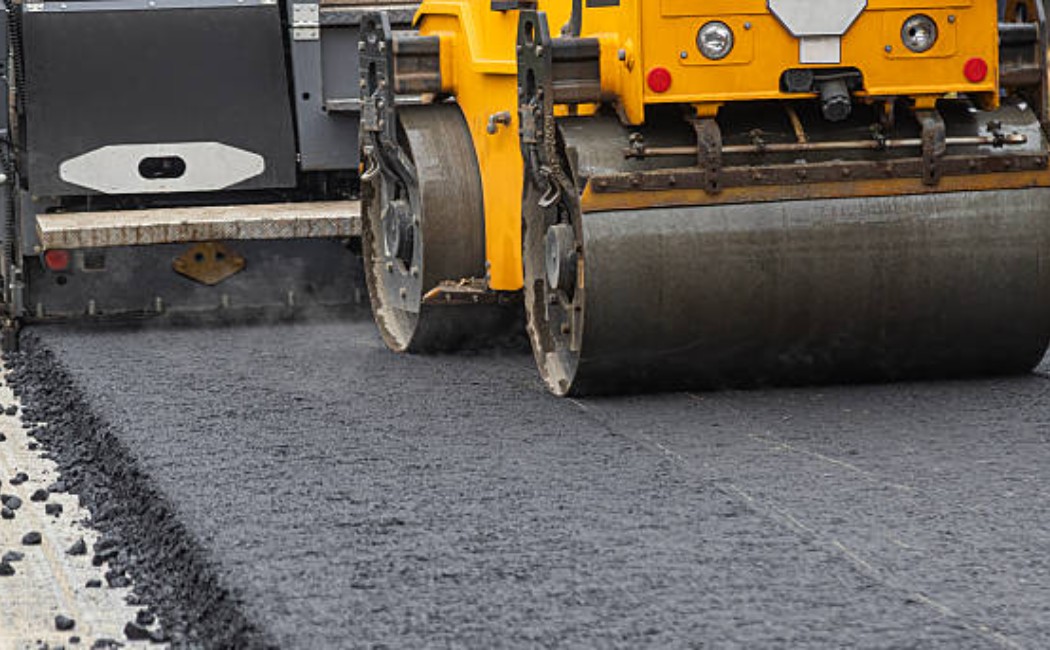 Heavy road paving machine laying fresh asphalt on highway construction