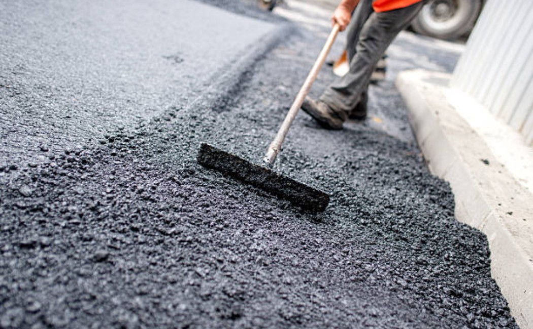 Asphalt paving at a construction site with a worker and tools.