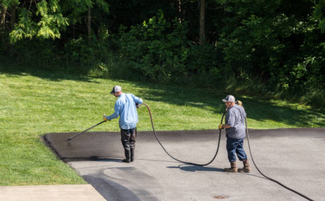 Workers in reflective clothing sealing a roadway surface.