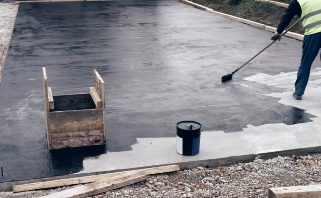 Construction site foundation receiving bitumen waterproofing with a hand tool.