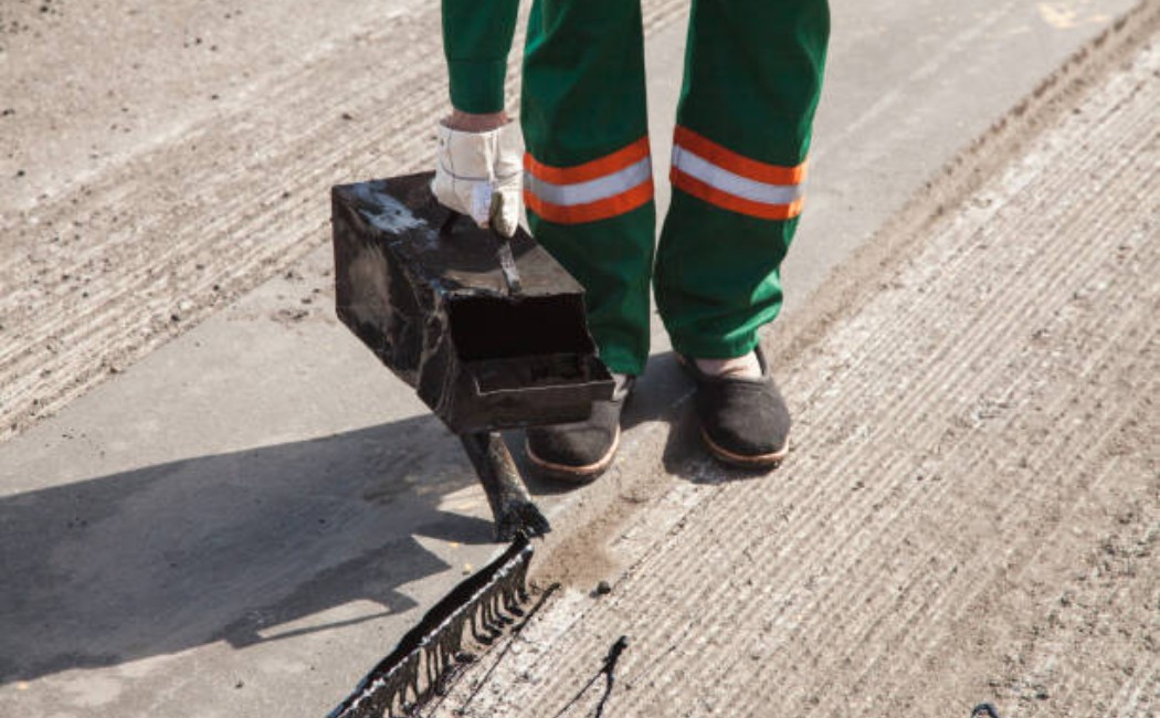 Worker pouring hot asphalt tar for road repair maintenance