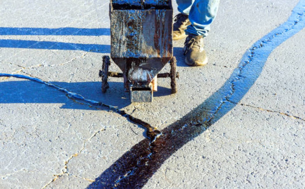 Road repair worker filling cracks on asphalt pavement.