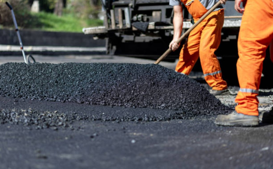 Asphalt paving machine and workers resurfacing a public road.