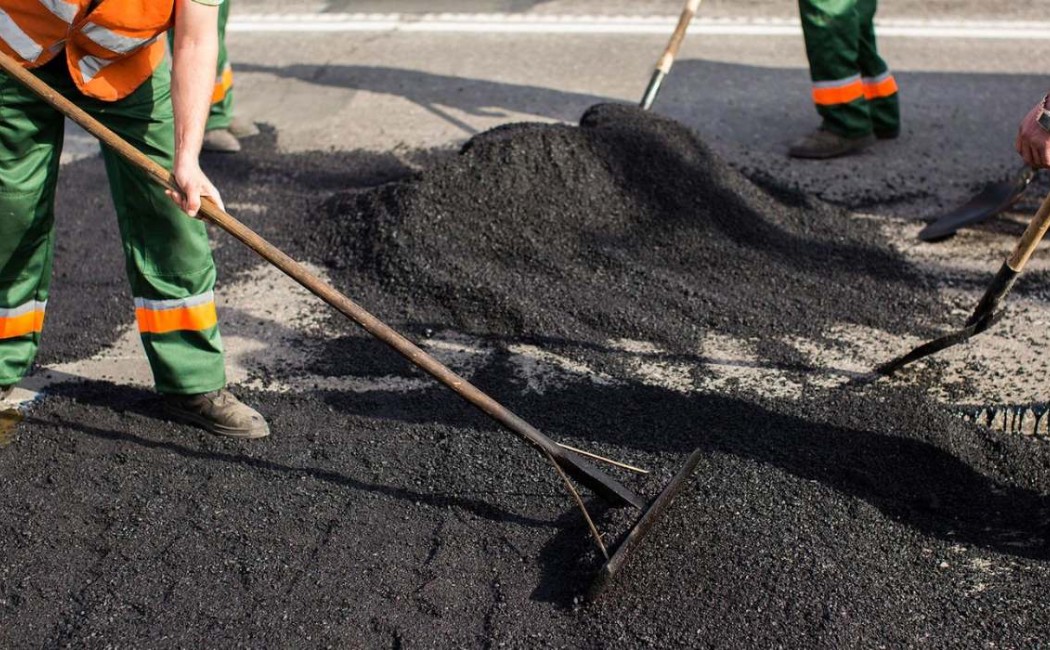 Asphalt Resurfacing Crew Leveling Fresh Asphalt on Roadway Asphalt Resurfacing workers spreading and leveling fresh asphalt with shovels on a worn roadway during repair work.