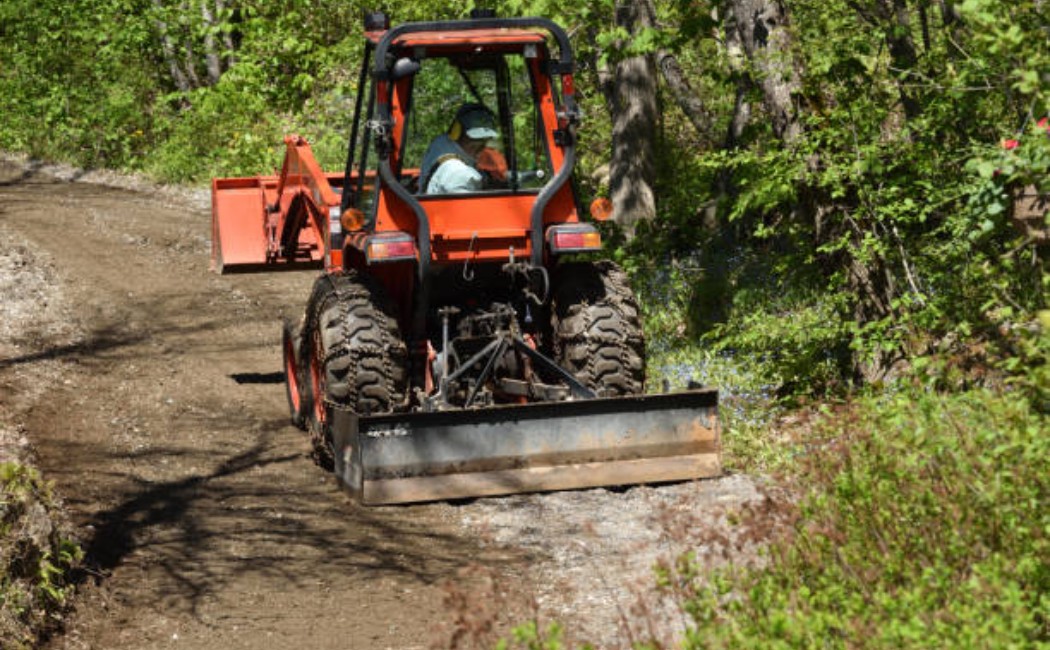Tractor smoothing out a dirt driveway on a farm.