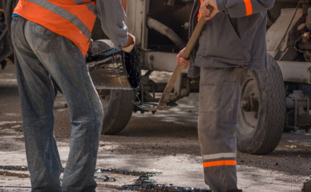 workers pouring resin on an asphalt road repair.
