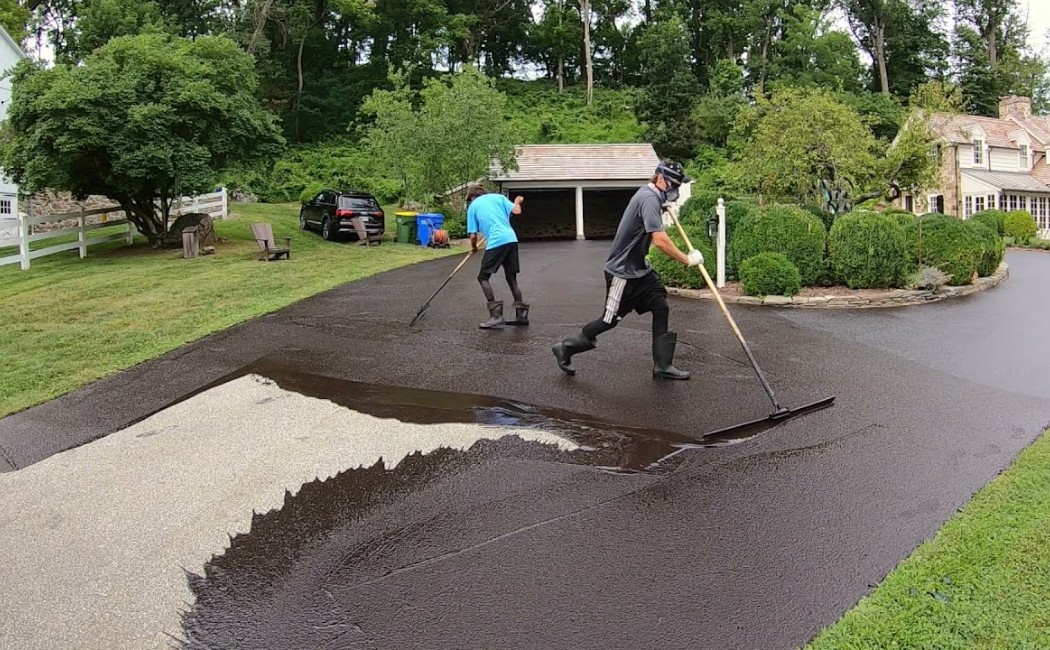 Edge-to-Edge Driveway Sealcoating Services for Lasting Protection Sealcoating Services being applied along the edge of a driveway, creating a smooth, dark protective layer against wear and weather.
