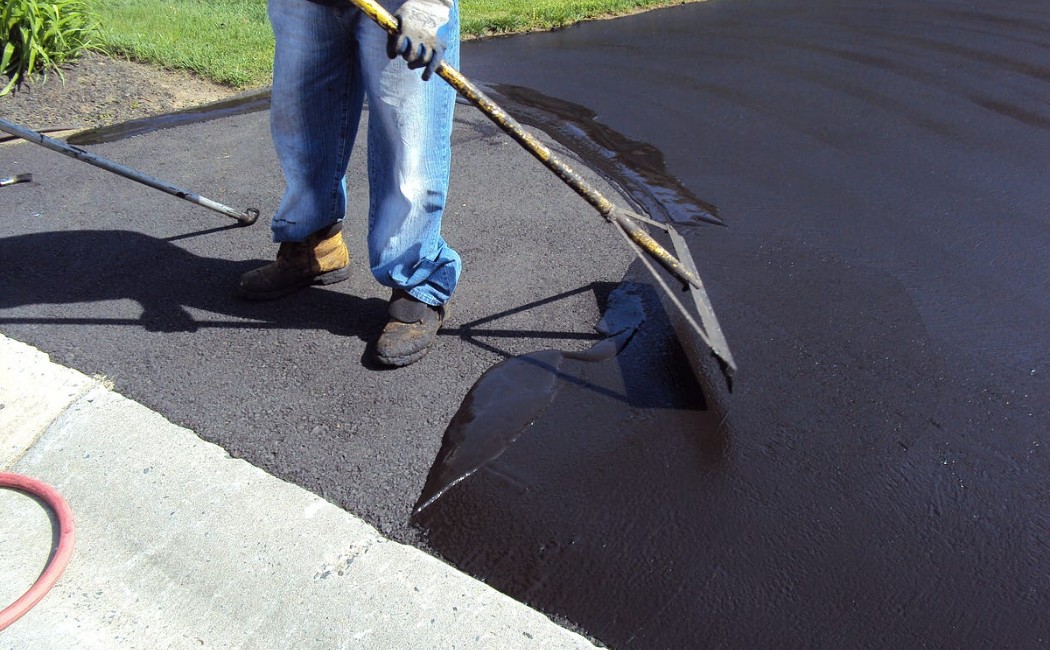 A professional applying protective coating to a residential driveway as part of Asphalt Sealcoating Services.