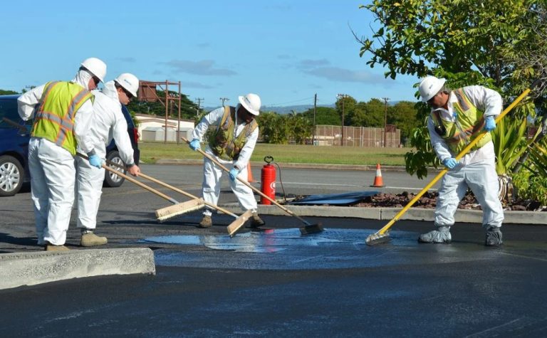 Workers in protective gear applying asphalt sealant during commercial Sealcoating Services in a parking lot.
