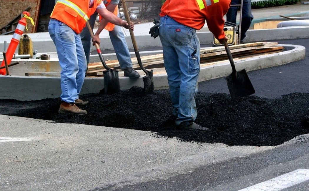 Asphalt Paving Maintenance workers using shovels to fill and repair a pothole with fresh asphalt on a city street.