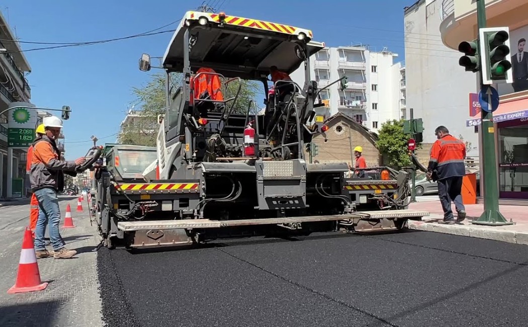Asphalt Paving Maintenance crew operating a road paving machine while laying fresh asphalt on a city street with workers and traffic cones.