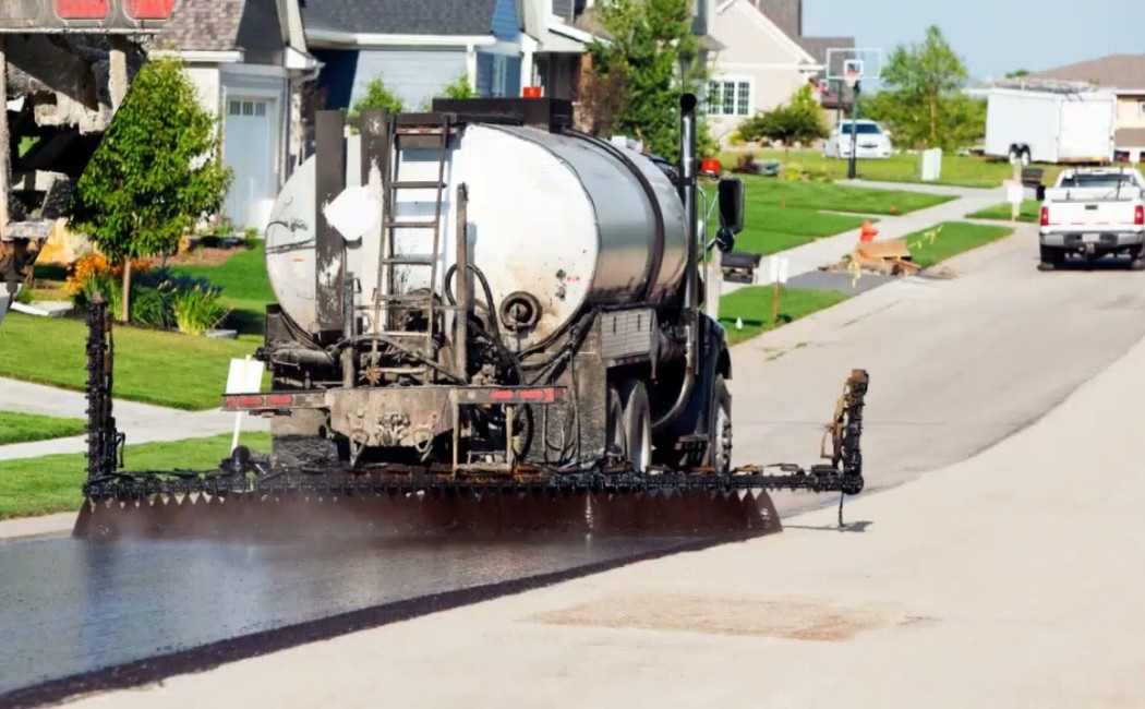 Truck applying fresh asphalt coating on a residential street during professional Sealcoating Services.