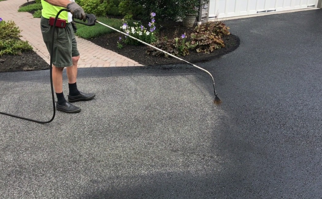 Technician sealing a residential asphalt driveway with spray equipment for professional Driveway Sealcoating Services.