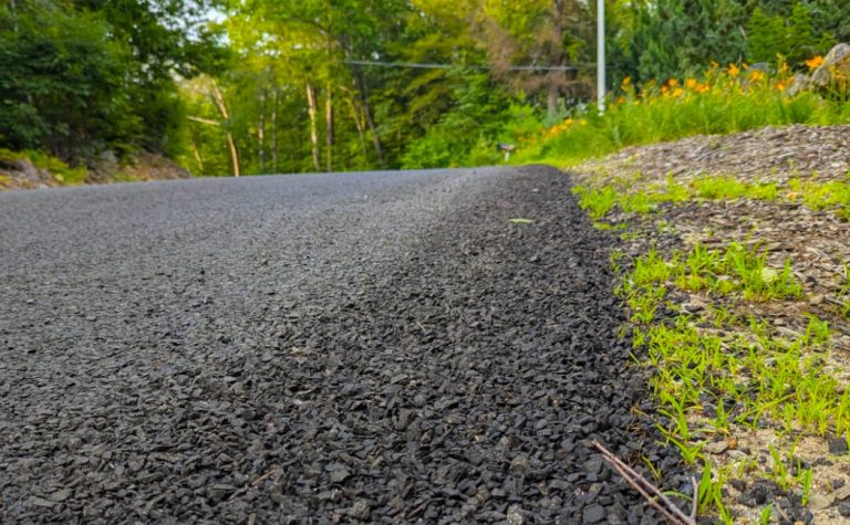 Chip Seal Driveways bordered by fresh grass and trees along a quiet rural road, showcasing a durable and textured paved surface.
