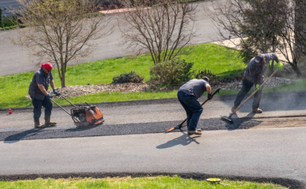 Workers repairing damaged asphalt road with fresh blacktop