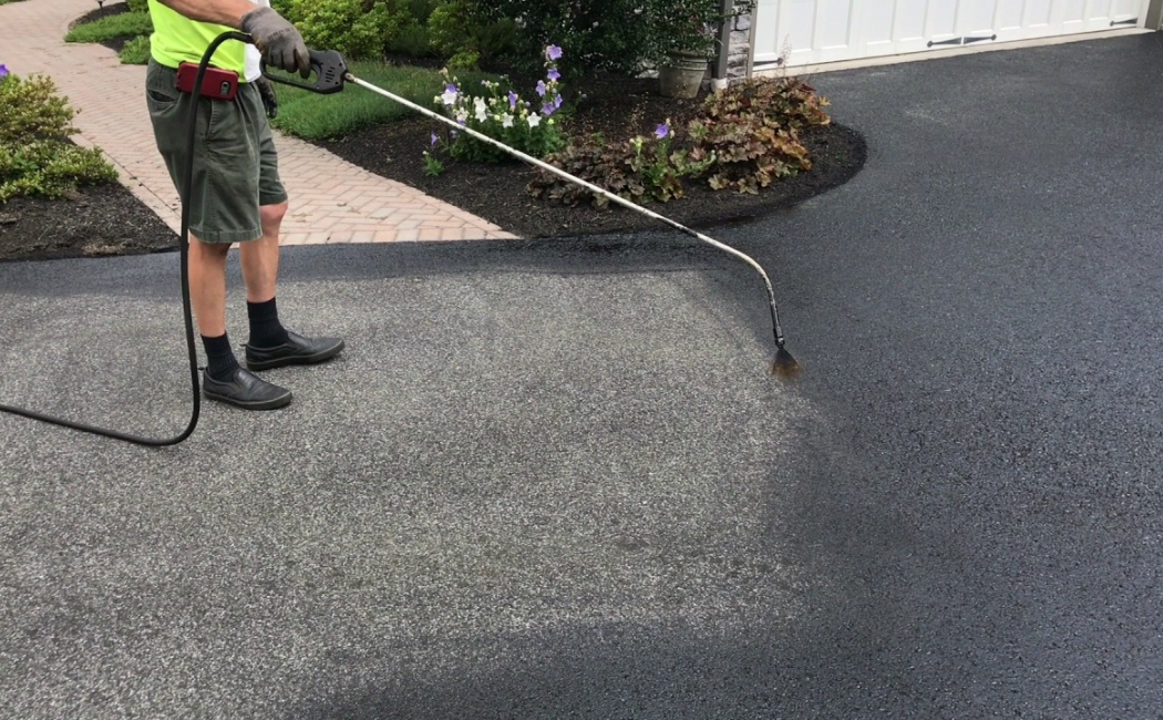 Seal Coating professional applying a protective seal coat to a residential asphalt driveway for enhanced durability and a smooth finished surface.