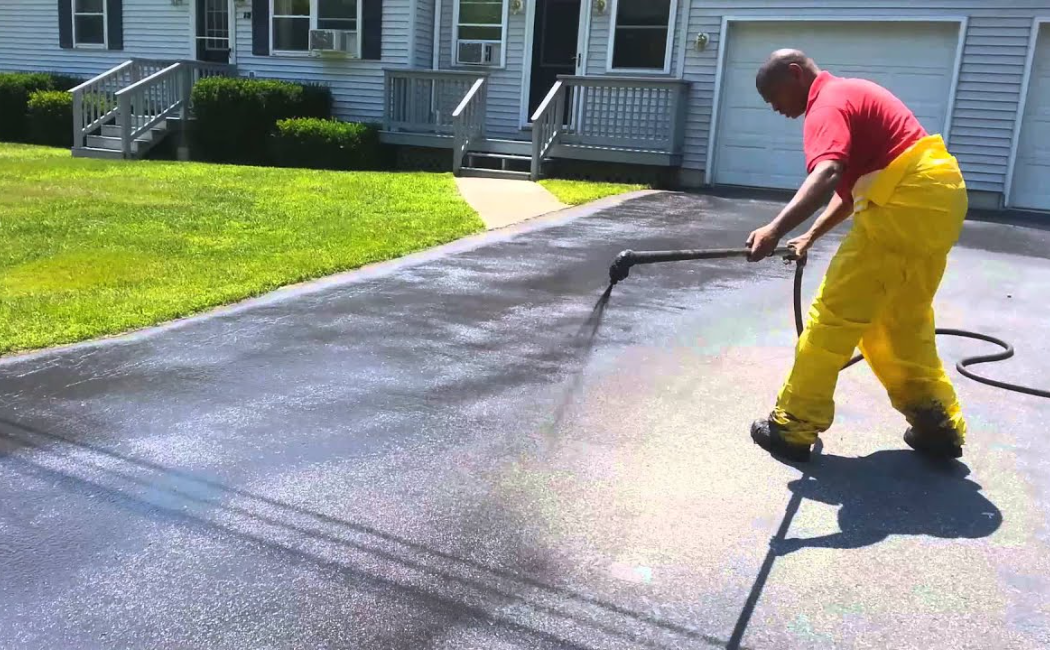 Residential Driveway Seal Coating Protection. Seal Coating contractor applying a protective asphalt seal coat to a residential driveway to improve durability, appearance, and weather resistance.