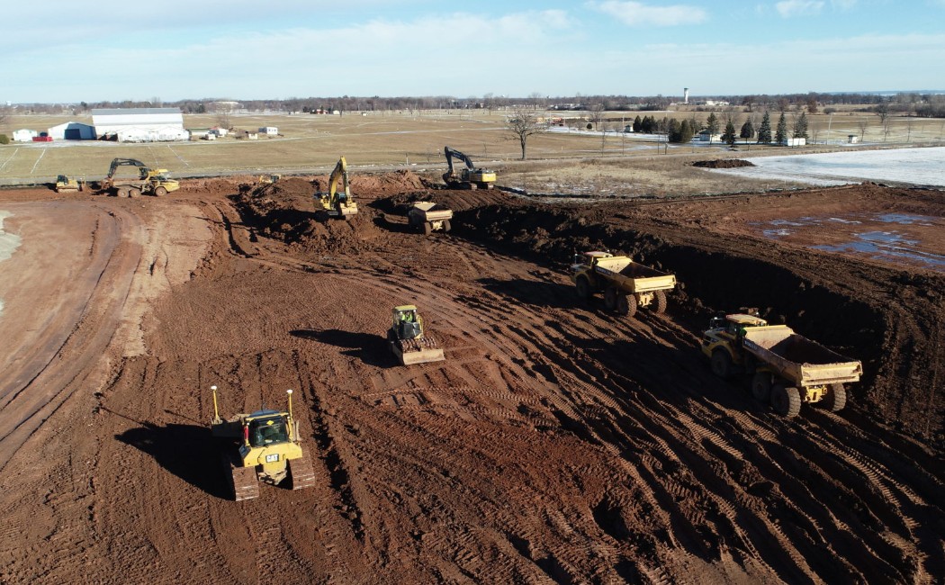 Grading project in progress with excavators, bulldozers, and dump trucks performing large-scale earthmoving and site preparation for future development.