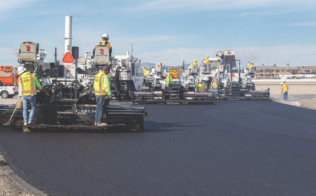 Construction crew performing asphalt paving with multiple paving machines laying fresh black asphalt on a wide roadway construction project.