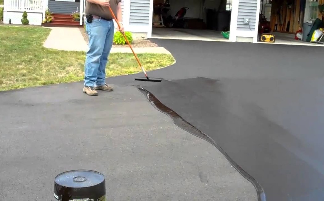 Asphalt Seal Coating for Residential Driveways. Worker spreading asphalt seal coating on a home driveway to restore its rich black appearance and extend pavement life.