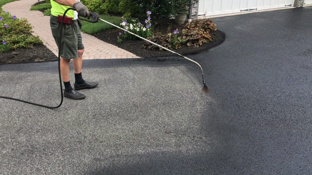 A professional applying Driveway Sealing Services to protect and restore a residential asphalt driveway.