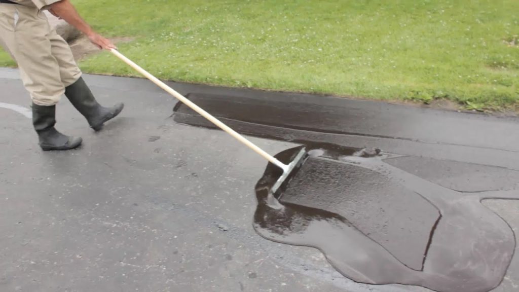 A worker spreads fresh asphalt sealer across a driveway for effective Driveway Sealing Services.