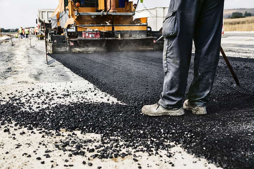 An asphalt maintenance crew is using a paving machine to lay fresh black asphalt on a road, ensuring a smooth, durable surface.