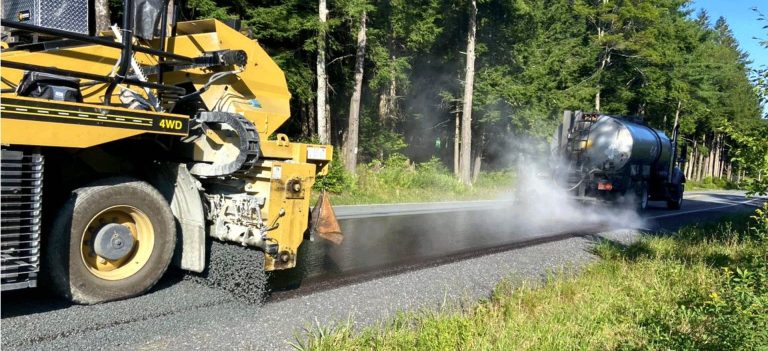 Chip Seal road paving machine applying hot asphalt and gravel to create a durable, weather-resistant road surface on a scenic forest highway.