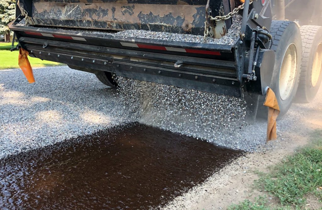 Chip Seal road resurfacing truck spreading crushed stone over fresh asphalt emulsion to create a durable, skid-resistant road surface for long-lasting pavement protection.