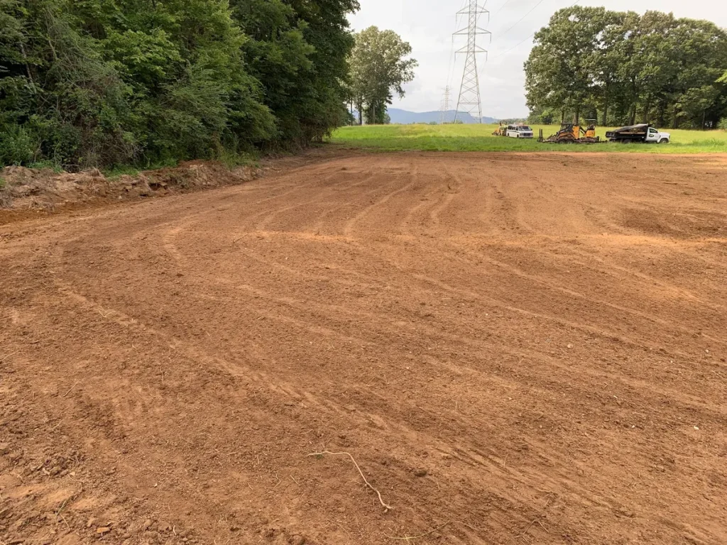 Yard grading levels uneven land with graded soil, equipment tracks, and a clear space ready for landscaping or construction.