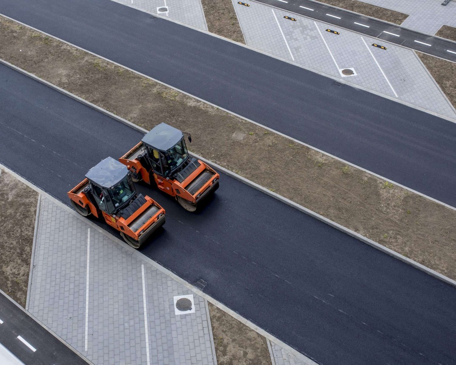 Aerial view of orange vibratory asphalt roller compactor on a new pavement